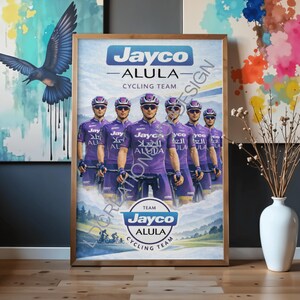 May include: A framed poster featuring the Jayco Alula Cycling Team. The image displays six cyclists in purple jerseys and helmets, positioned above a landscape with a circular logo that reads Team Jayco Alula Cycling Team in blue and white.