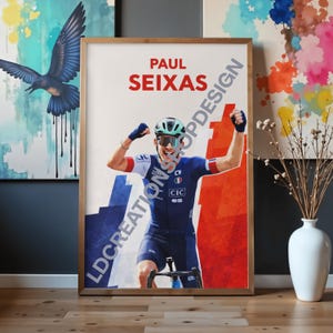 Peut inclure: Une affiche encadrée représentant le cycliste Paul Seixas en maillot bleu et blanc avec des accents rouges, portant un casque et des lunettes, les bras levés en signe de victoire. Fond avec formes abstraites bleu et rouge et texte LDCREATIONSDESIGN.