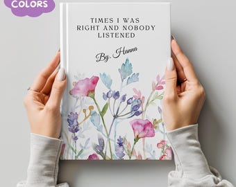 May include: A white journal with the text "TIMES I WAS RIGHT AND NOBODY LISTENED" and "By. Hanna". The cover features watercolor floral illustrations in pink, purple, and blue. A purple bubble with the words "MORE COLORS" is in the upper left corner.