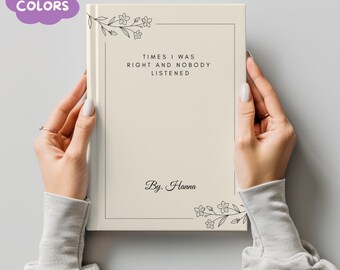 May include: A cream-colored journal held by two hands. The cover features the text "TIMES I WAS RIGHT AND NOBODY LISTENED" within a black border, with floral accents. The journal is signed "By. Hanna". A purple cloud-shaped text bubble reads "MORE COLORS".