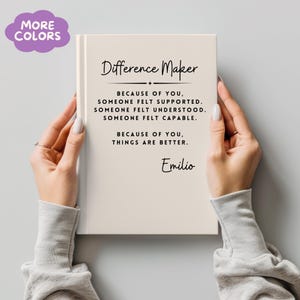 Puede incluir: Un diario de color crema con las palabras "Difference Maker" y texto inspirador. El diario incluye el nombre "Emilio" en la parte inferior. Una burbuja morada con las palabras "MORE COLORS" está en la esquina superior izquierda.
