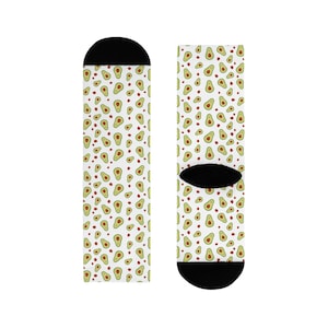 Könnte beinhalten: Socken mit weißem Hintergrund und einem sich wiederholenden Muster aus Avocados und kleinen roten Samen. Die Socken haben schwarze Fersen und Zehen.