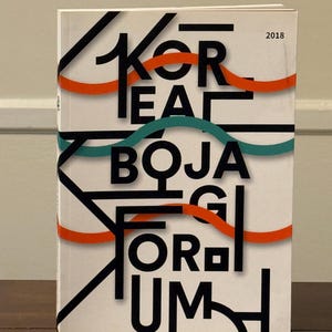 May include: A white book cover featuring the black text KOREA BOJAGI FORUM 2018. The design includes bold black geometric lines and overlapping wavy horizontal bands in orange and teal that intersect with the typography across the front cover.