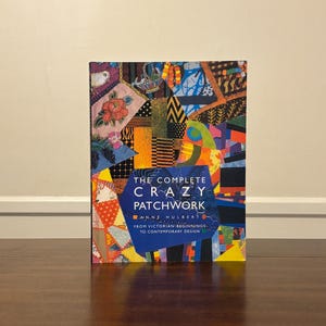 May include: A hardcover book titled The Complete Crazy Patchwork by Anne Hulbert. The cover features a vibrant, multi-colored collage of various fabric patterns, textures, and embroidery designs, with a central blue shape containing the title text.