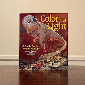 May include: A hardcover book titled Color and Light: A Guide for the Realist Painter by James Gurney, creator of Dinotopia. The cover features a detailed illustration of a feathered, bird-like dinosaur standing on a rocky, textured ground.