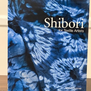 Può includere: Un libro intitolato "Shibori for Textile Artists" con una copertina blu e bianca con motivo tie-dye. Il titolo è in bianco e il nome dell'autore, Janice Gunner, è in basso. Per artisti tessili.