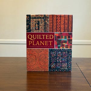 Puede incluir: Un libro titulado "Quilted Planet" con una portada roja y patrones de patchwork coloridos. El libro, de Celia Eddy, es una fuente de inspiración sobre edredones de todo el mundo. La portada es multicolor.