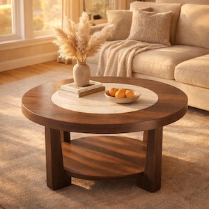May include: A circular coffee table made of dark wood, featuring a light marble centre. It has a lower shelf and is adorned with a vase of dried flowers, books, and a bowl of oranges. The table is a focal point in a living room setting.