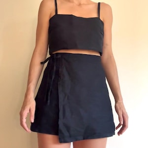 Peut inclure: Ensemble deux pièces noir composé d'un crop top à fines bretelles et d'une jupe portefeuille. La jupe s'enroule autour de la taille et se noue sur le côté. L'ensemble est en tissu uni et foncé.