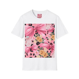 Könnte beinhalten: Weißes T-Shirt mit einem Muster aus rosa Schleifen und Blumen. Das Design zeigt rosa Schleifen, Rosen und einen Parfümflakon auf einem rosa Leopardenmuster. Das T-Shirt hat einen Rundhalsausschnitt und kurze Ärmel.