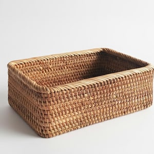 Könnte beinhalten: Ein rechteckiger Webkorb in natürlicher, hellbrauner Farbe. Der Korb besteht aus dicht gewebtem Material mit einem leicht abgerundeten Rand. Der Korb ist leer und steht auf einer weißen Oberfläche.
