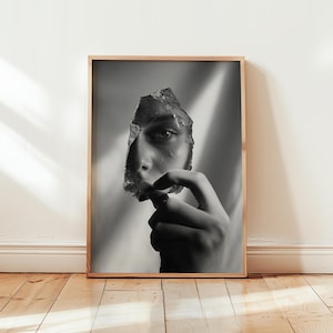 Könnte beinhalten: Schwarz-Weiß-Kunstdruck in einem Holzrahmen, der ein Gesicht zeigt, das teilweise von einem Glassplitter verdeckt wird. Das Auge der Person ist durch das Glas sichtbar. Das Kunstwerk ist in einem Holzrahmen präsentiert.