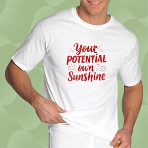 Könnte beinhalten: Weißes T-Shirt mit dem roten Text "Your Potential Own Sunshine". Das kurzärmelige T-Shirt scheint aus einem weichen Material zu sein. Das Design ist mittig auf der Brust platziert.