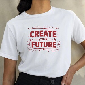 May include: White t-shirt with the red text "CREATE YOUR FUTURE" in a decorative font. The design is centered on the shirt, with the words arranged in two lines. The shirt is a casual, everyday wear item.