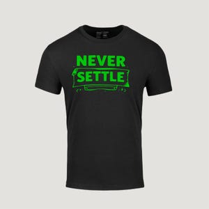 Può includere: T-shirt nero girocollo con la scritta "NEVER SETTLE" in verde brillante, bordata di un verde leggermente più scuro. Il testo è centrato sul davanti della maglietta, all'interno di un disegno a banner verde.