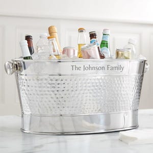 May include: A stainless steel beverage tub filled with ice and various bottles and cans. The tub has a hammered texture and the text "The Johnson Family" is engraved on the side. The tub has two handles.