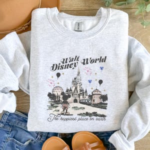 May include: Light gray sweatshirt with a graphic of Cinderella's castle, Mickey Mouse, and the text "Walt Disney World" and "The happiest place on earth". The design includes fireworks and balloons.