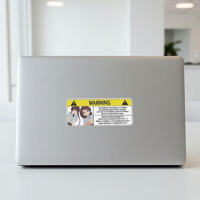 May include: A rectangular sticker with a yellow and black warning label. The label features anime-style illustrations of two girls and text in English and Japanese. The text warns about the vehicle owner's behavior.