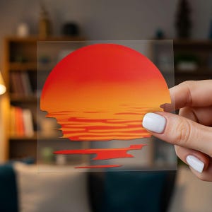 Può includere: Un adesivo a tema tramonto con una sfumatura di rosso e arancione. Il design raffigura un sole stilizzato che tramonta sull'acqua, con bordi frastagliati nella parte inferiore. L'adesivo è tenuto in mano.