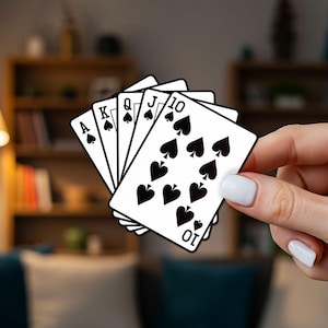 Könnte beinhalten: Ein Blatt Spielkarten mit dem Ass, König, Dame, Bube und 10 Pik. Die Karten sind weiß mit schwarzen Pik-Symbolen und Text. Der Hintergrund ist unscharf, was auf eine Innenaufnahme hindeutet.