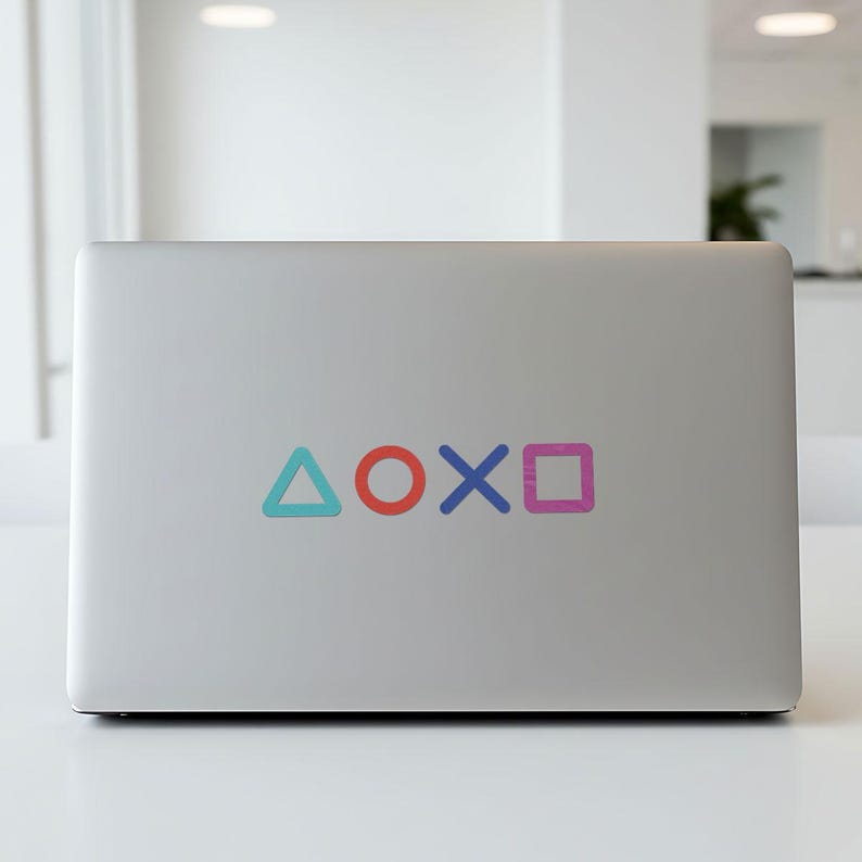 Puede incluir: Un port&aacute;til plateado con una pegatina que muestra los s&iacute;mbolos del mando de PlayStation: un tri&aacute;ngulo azul, un c&iacute;rculo rojo, una X azul y un cuadrado rosa. Los s&iacute;mbolos est&aacute;n dispuestos horizontalmente.
