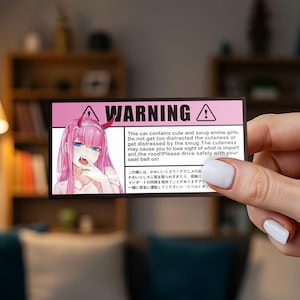 May include: A rectangular sticker with a pink background and the word "WARNING" in black. It features an anime girl with pink hair and text warning about distractions. The sticker also includes Japanese text.