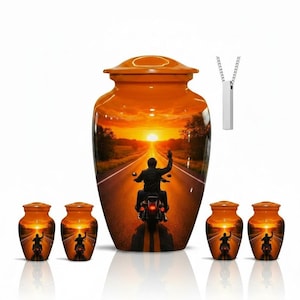 May include: A large orange cremation urn and four smaller matching keepsake urns, each featuring a sunset road scene with a motorcyclist waving. A silver-toned rectangular pendant on a chain is positioned above the large central urn.
