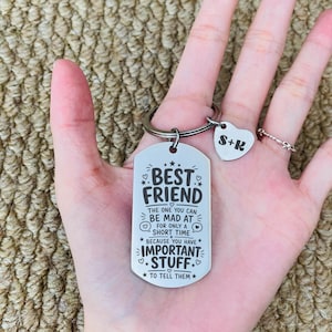 May include: A silver-toned metal dog tag keychain featuring the engraved text: BEST FRIEND THE ONE YOU CAN BE MAD AT FOR ONLY A SHORT TIME BECAUSE YOU HAVE IMPORTANT STUFF TO TELL THEM. A small heart-shaped charm with the letters S+R is attached.