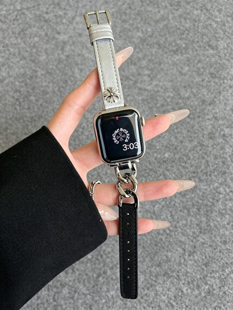 May include: Silver Apple Watch with a silver leather band and a black leather strap. The watch face displays the time as 3:03. The band features a decorative floral design.