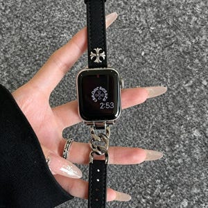 May include: Black Apple Watch with a silver chain band and a black fabric strap. The watch face displays the time as 2:53. The band features a silver cross design.