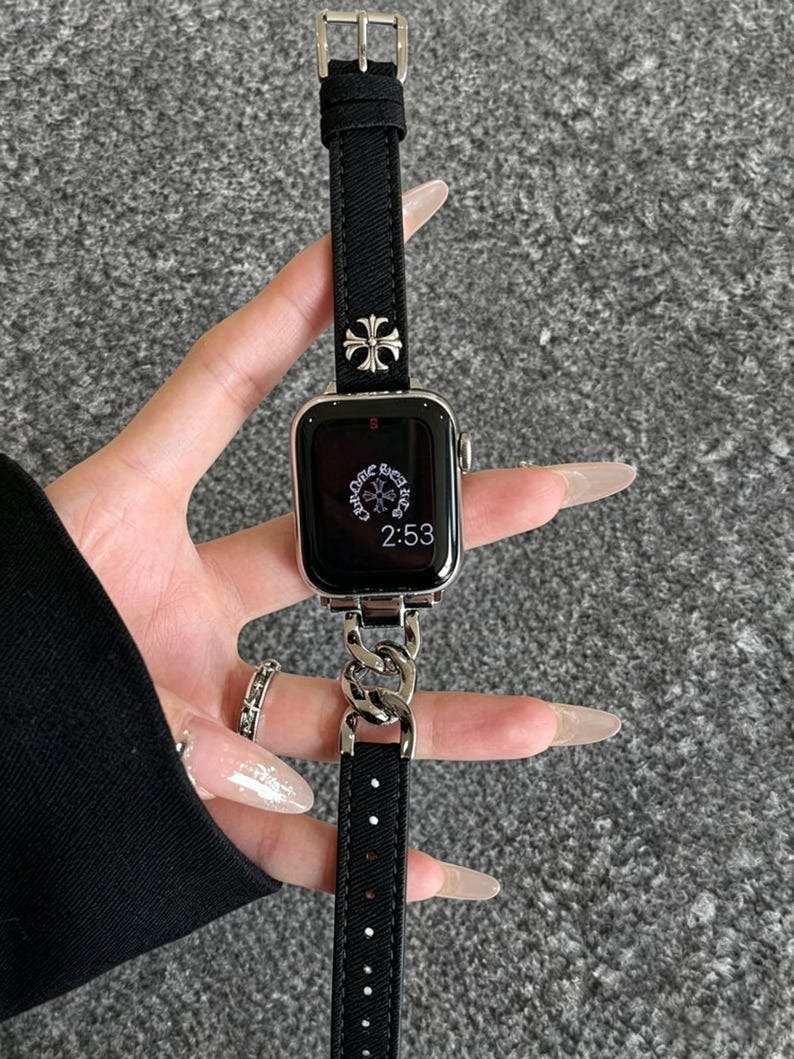 May include: Black Apple Watch with a silver chain band and a black fabric strap. The watch face displays the time as 2:53. The band features a silver cross design.