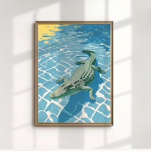 May include: A framed art print featuring a green alligator floating in a blue swimming pool. The pool has a white tile pattern and the water reflects yellow sunlight. The artwork is in a gold frame.