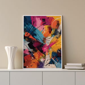 Puede incluir: Impresión artística abstracta con borde blanco. La obra presenta una vibrante mezcla de colores, incluyendo azul, naranja, rosa, amarillo y negro, con pinceladas y salpicaduras audaces. La pintura se exhibe en una estantería blanca.
