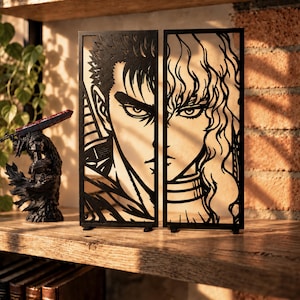Puede incluir: Dos paneles rectangulares negros cortados con láser que presentan retratos estilizados de dos personajes. El panel izquierdo muestra a un personaje de pelo corto con mirada intensa, el derecho a uno de pelo largo con ondas.