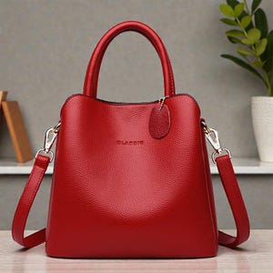 Può includere: Una borsa rossa con un manico superiore e una tracolla staccabile. La borsa ha una superficie strutturata e hardware color oro. La parola "CLASSIC" è stampata sulla parte anteriore della borsa.
