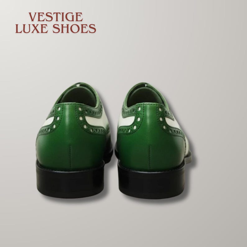 May include: A pair of green and white wingtip shoes with black heels and soles. The text VESTIGE LUXE SHOES is printed in dark red in the upper left corner. The shoes feature decorative brogue perforations along the leather panels.