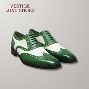 May include: A pair of green and white wingtip oxford shoes with black laces and brogue detailing. The text VESTIGE LUXE SHOES is printed in dark red in the upper left corner. The shoes feature a two-tone leather design with a black sole.