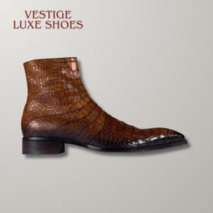 May include: A brown ankle boot with a textured crocodile skin pattern and a dark brown heel. The text VESTIGE LUXE SHOES is printed in dark red above the boot. The boot features a pointed toe and a smooth, dark brown sole.