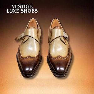 Könnte beinhalten: Zweifarbige Lederschuhe mit Schnallenverschluss. Die Schuhe haben ein hellbeige Obermaterial und eine dunkelbraune Spitze und Ferse. Der Text "VESTIGE LUXE SHOES" steht oben.