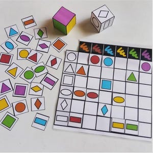 Peut inclure: Un jeu éducatif coloré avec des formes géométriques. Il comprend un plateau de jeu, des cartes de formes et deux dés. Les dés sont en forme de cube, l'un avec des faces colorées et l'autre avec des contours de formes. Les cartes et le plateau présentent diverses formes de différentes couleurs.