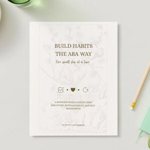 Può includere: Un libro color crema intitolato "BUILD HABITS THE ABA WAY" con decorazioni floreali. Sono visibili anche una matita, un piccolo taccuino verde e un grappolo d'uva. Il sottotitolo del libro è "One small step at a time."