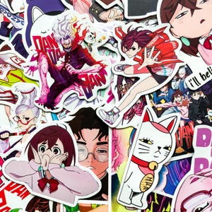 Könnte beinhalten: Eine Sammlung farbenfroher Aufkleber im Anime-Stil mit verschiedenen Charakteren und Designs. Die Aufkleber zeigen eine Vielzahl von Posen und Ausdrücken, mit leuchtenden Farben und detaillierten Kunstwerken. Einige Aufkleber haben japanischen Text.