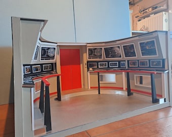May include: A model of a futuristic interior, possibly a spaceship bridge, with a curved console, multiple display screens, and a red door. The color scheme includes gray, black, and red accents.