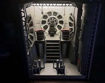 May include: A detailed diorama of a spaceship interior, featuring a central command chair, stairs, and circular windows. The scene is lit with internal lighting, highlighting the intricate details and textures of the model. The color palette is primarily gray and white.