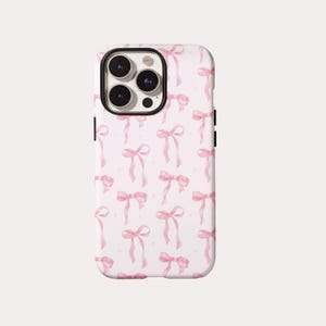 May include: A light pink smartphone case featuring a repeating pattern of watercolor-style pink bows. The case has a rectangular shape with rounded corners and a large circular cutout at the top left for the camera lenses and flash module.