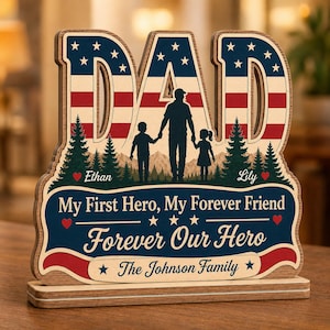 May include: A wooden tabletop sign shaped like the word DAD with a red, white, and blue American flag pattern. It features a silhouette of a parent and two children, pine trees, mountains, and the text My First Hero, My Forever Friend, Forever Our Hero.