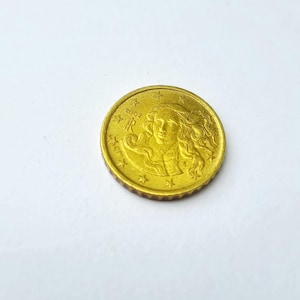 Peut inclure: Une pièce de 10 centimes d'euro italienne de couleur dorée représentant en relief la Naissance de Vénus de Sandro Botticelli. La pièce affiche l'année 2002, le monogramme IR pour la République italienne et une série d'étoiles sur le bord.