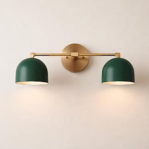 May include: A wall-mounted light fixture with a brass finish and two dark green dome shades. The sconce features a circular backplate and a horizontal bar. The shades are approximately 15 cm in diameter.
