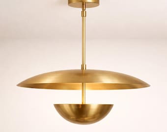 May include: A brass-colored, mid-century modern pendant light fixture. The fixture has a circular ceiling mount, a long central rod, and a large, shallow, saucer-shaped shade above a smaller, bowl-shaped shade. The light is suspended from the ceiling.