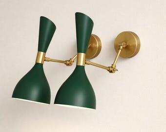 Może przedstawiać: Dwa kinkiety ścienne o nowoczesnym designie z połowy wieku. Każdy kinkiet ma ciemnozielony, dzwonkowaty klosz oraz mosiężne ramię i mocowanie do ściany. Klosze są ustawione pod kątem, a kinkiety są zamontowane na białej ścianie.